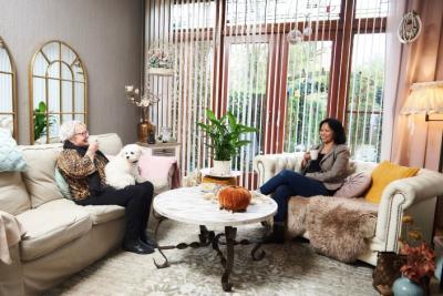 Thuishulp en haar client samen aan de koffie in de huiskamer. Client heeft haar hondje op schoot.