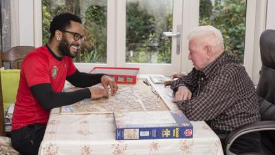 Thuishulp en klant die samen een spelletje spelen aan de eettafel Thuishulp en klant die samen een spelletje spelen aan de eettafel