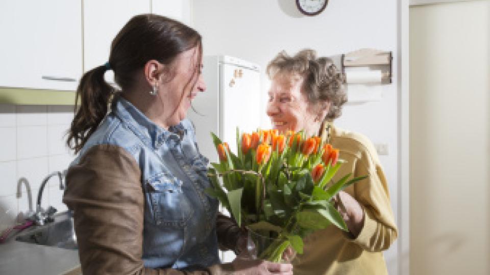 Thuishulp en klant in keuken van mevrouw met bos bloemen.